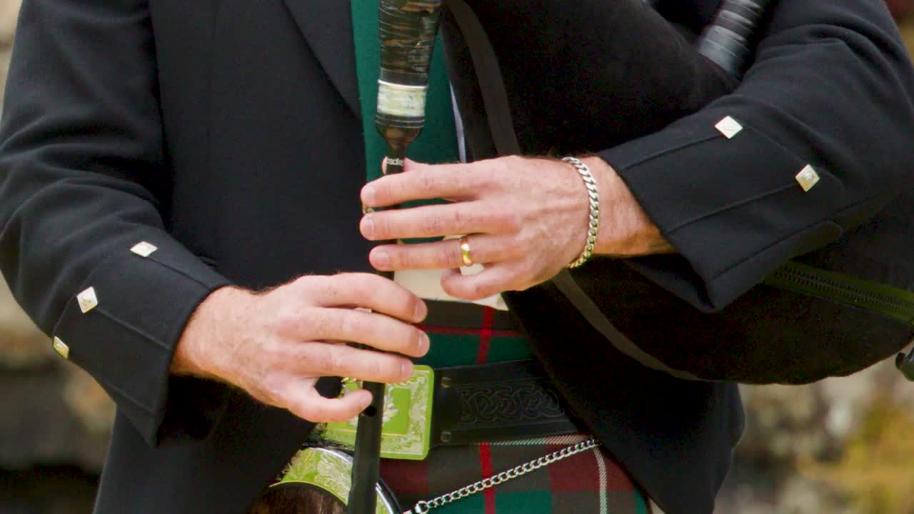 Detailed midsection view of a musician's hands playing bagpipes wearing a kilt and jacket