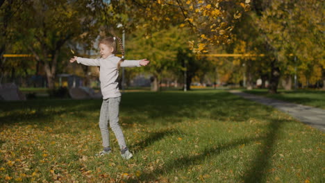 Playful-preschooler-girl-dances-scattering-yellow-leaves