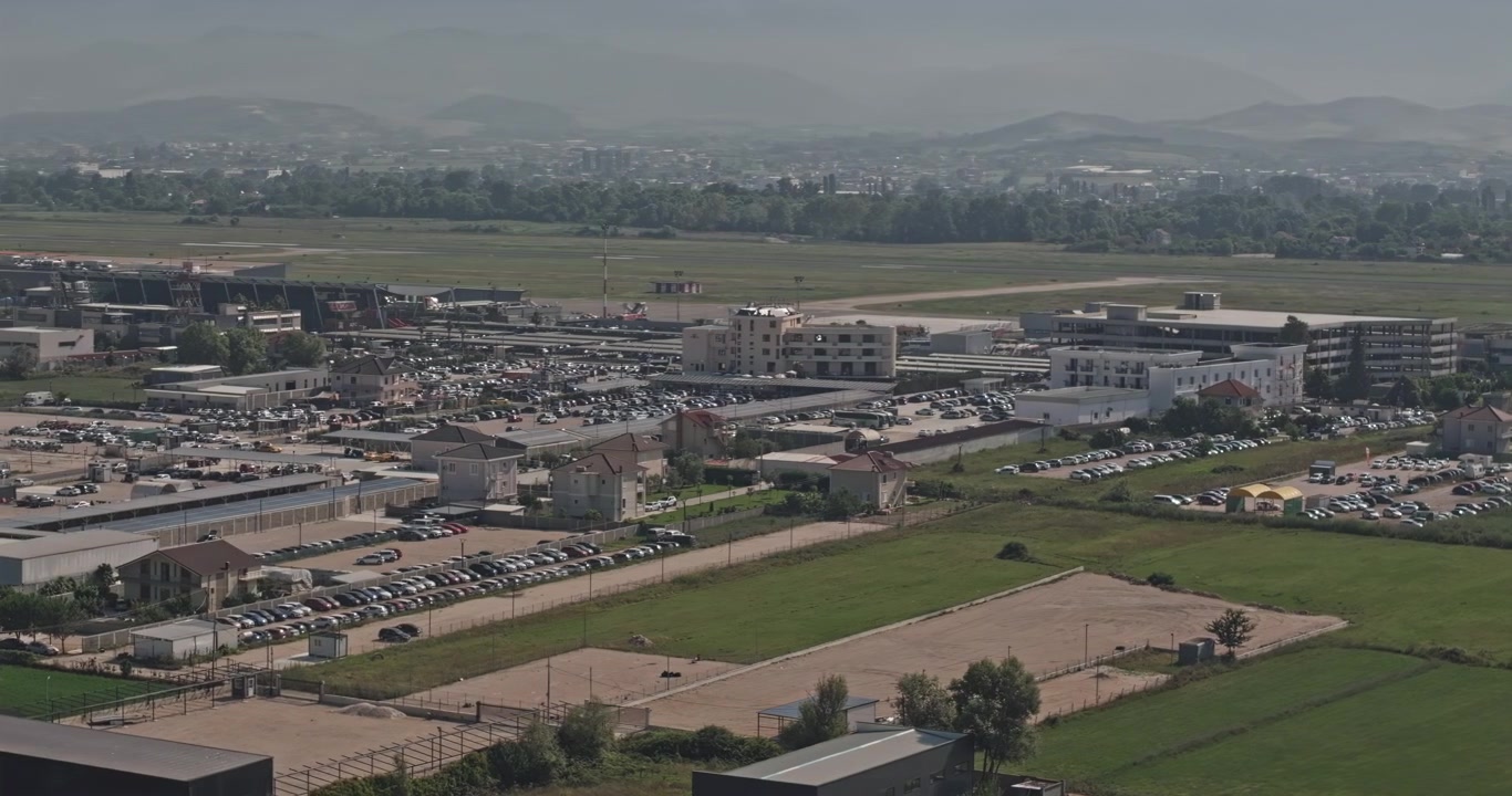 Sorvolo a bassa quota con teleobiettivo, Tirana Albania Aerea v6, che rivela la pista dell'Aeroporto Internazionale di Tirana, il quartiere dei terminal e i parcheggi dei veicoli oltre i campi agricoli di Rinas - Scattato con Mavic 3 Pro Cine - 10 luglio 2024