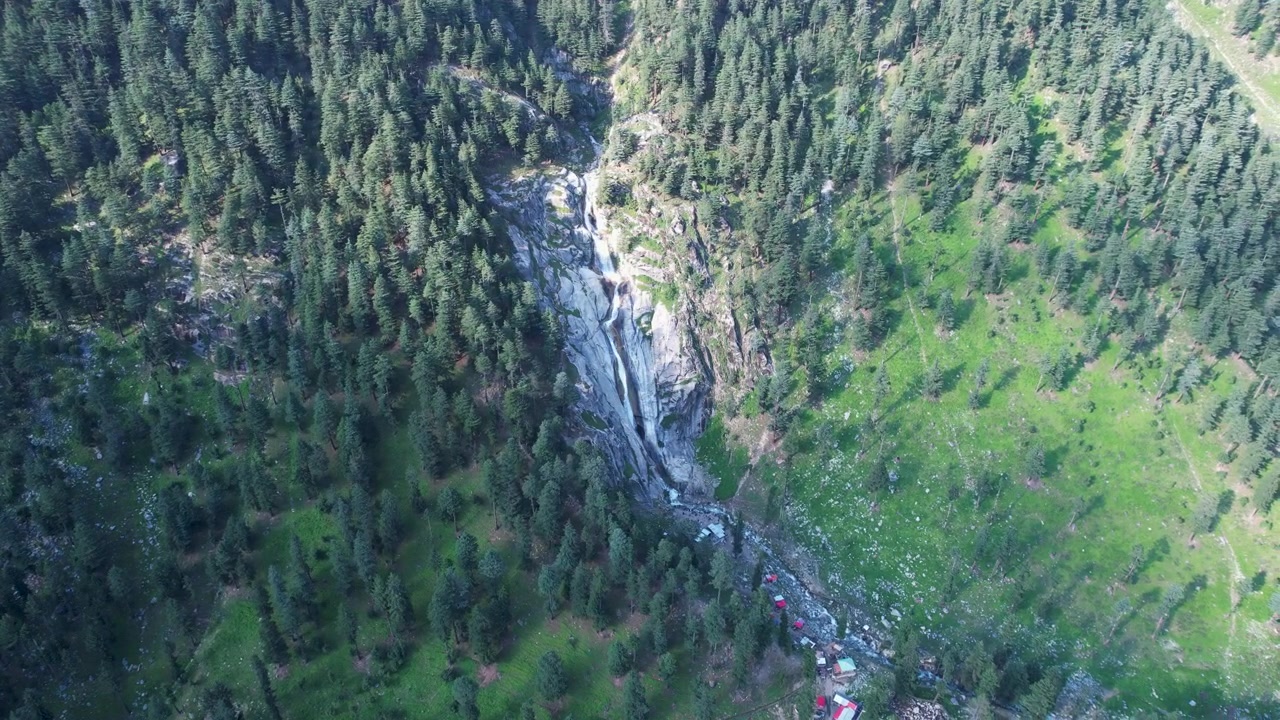 Una cascata scende attraverso una fitta pineta su un pendio di montagna nella Valle di Kumrat, Khyber Pakhtunkhwa, Pakistan.