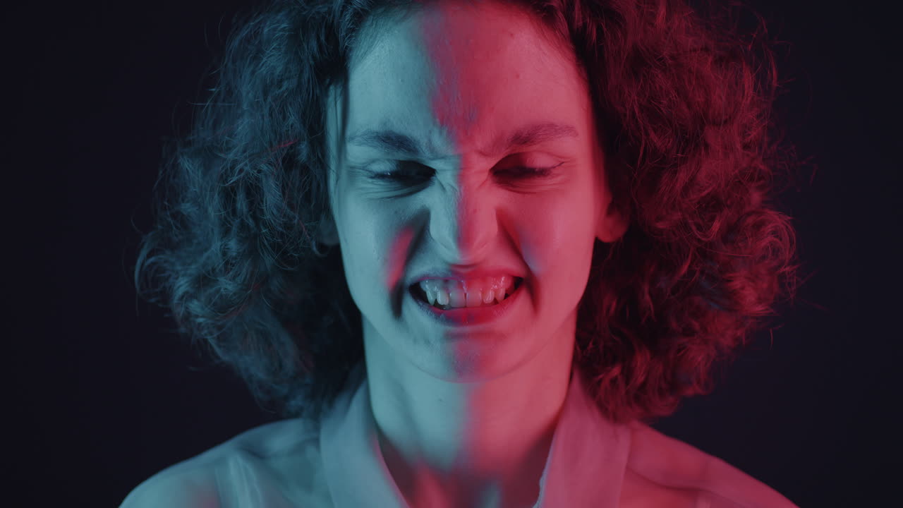 Close-up of a woman with a displeased expression, illuminated in neon blue and red light.
