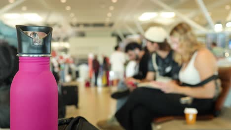 a pink bottle in focus at an airport, with blurred passengers in the background, creating a dynamic depth of field