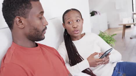 African-american-couple-sitting-up-in-bed,-using-smartphones-and-talking,-in-slow-motion