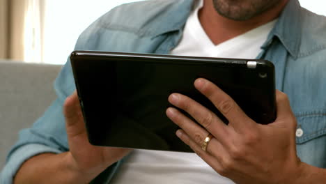 Mid-section-of-man-using-tablet-on-the-sofa