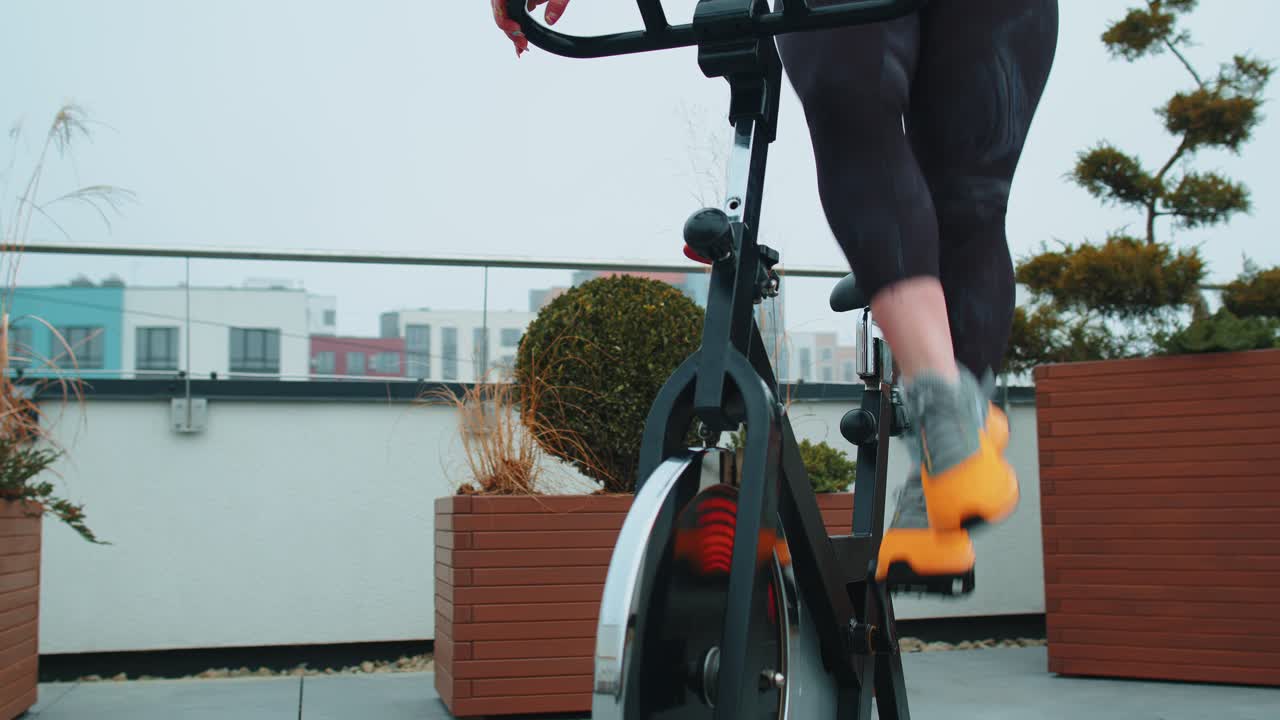 Athletic woman riding on spinning stationary bike training routine on house rooftop weight loss