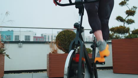 athletic woman riding on spinning stationary bike training routine on house rooftop weight loss