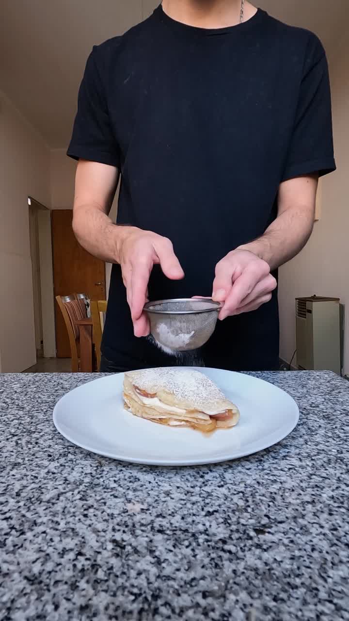 disparo vertical de un hombre terminando un postre de crepe añadiendo azúcar en polvo