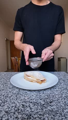 vertical shot of a man finishing a crepe dessert by adding powdered sugar