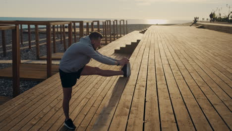 man stretching on a wooden beach deck at sunset