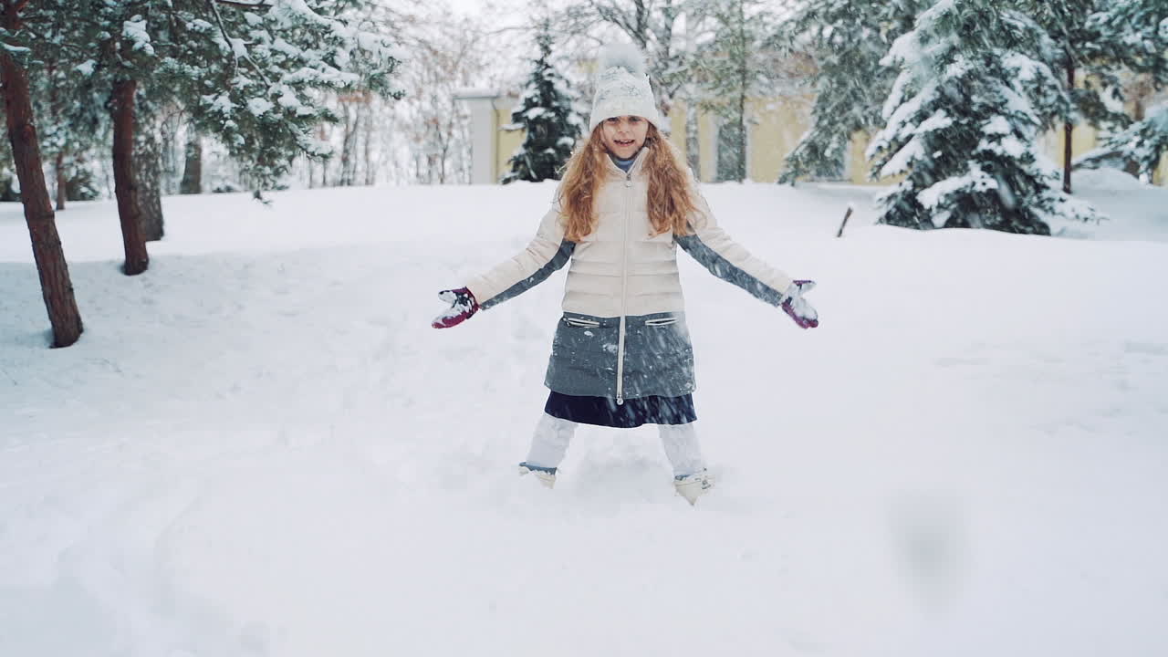 Happy girl playing in snow. Girl in knitted hat making snowflakes in winter park