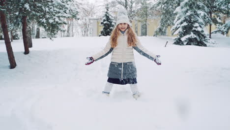 happy girl playing in snow. girl in knitted hat making snowflakes in winter park