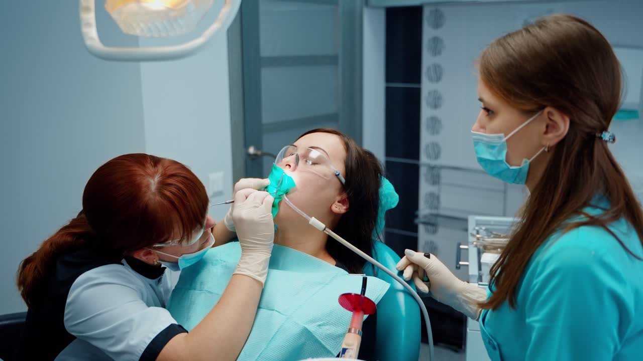Woman visits stomatologist. Dentist and assistant treat patient's tooth in modern dental office. Female professional stomatologist at work.