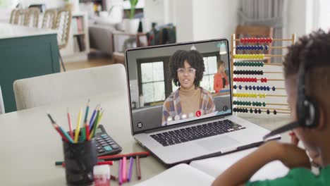 niño afroamericano usando una computadora portátil para una lección en línea con una maestra afroamericana en la pantalla
