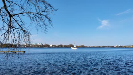 a white sailboat slowly moves across the calm alster lake in hamburg on a sunny day