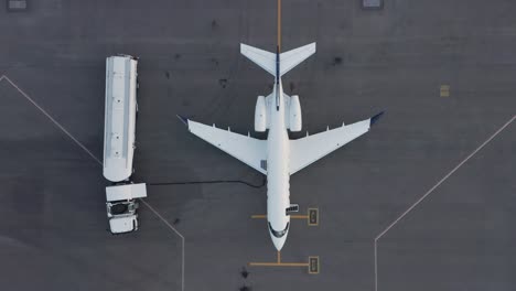 Top-down-aerial-of-business-jet-parked-on-tarmac-getting-fuel-pumped-into-tanks