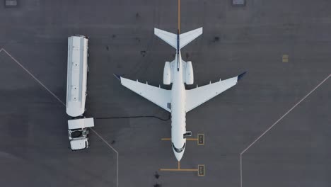 top down aerial of business jet parked on tarmac getting fuel pumped into tanks