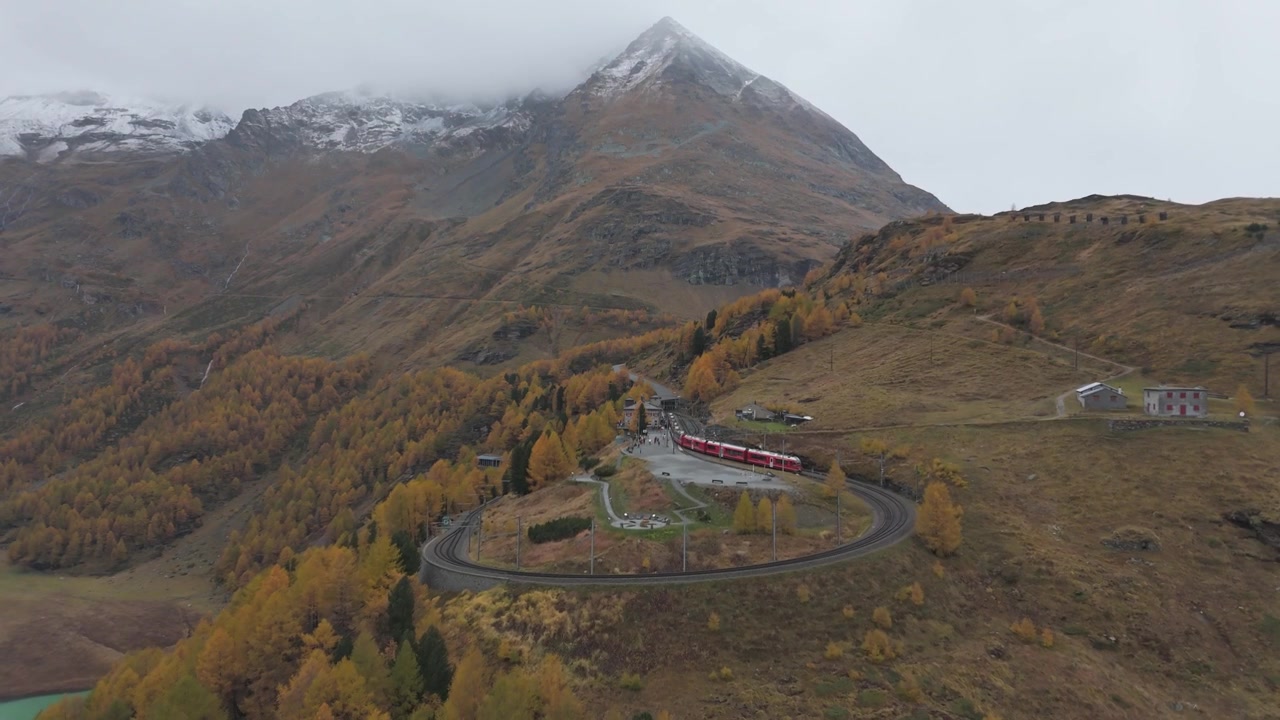 Una pittoresca ferrovia alpina si snoda attraverso il vivace paesaggio autunnale vicino ad Alp Grüm, Grigioni, Svizzera. La scena presenta un treno, fogliame colorato e aspre vette montuose.