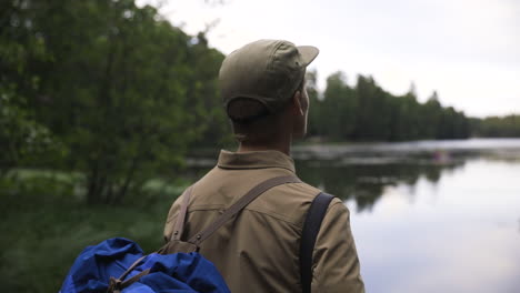 Close-view-of-young-man-looking-out-on-lake-and-forest,-slow-pan