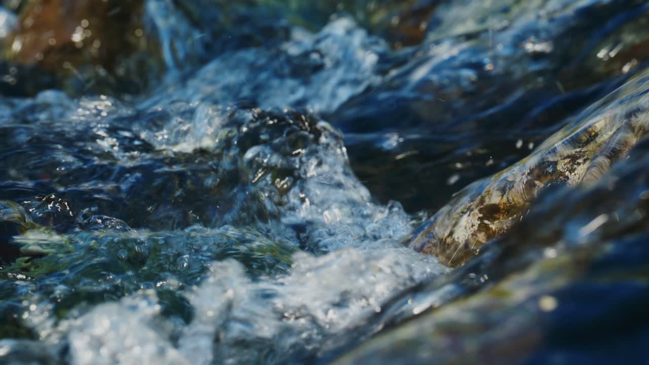 Água límpida corre rapidamente sobre as rochas. A luz do sol brilha nas ondulações da superfície. Texturas naturais e movimento dinâmico. Ideal para projetos de natureza, viagem ou ambientais. Sem pessoas ou animais presentes.