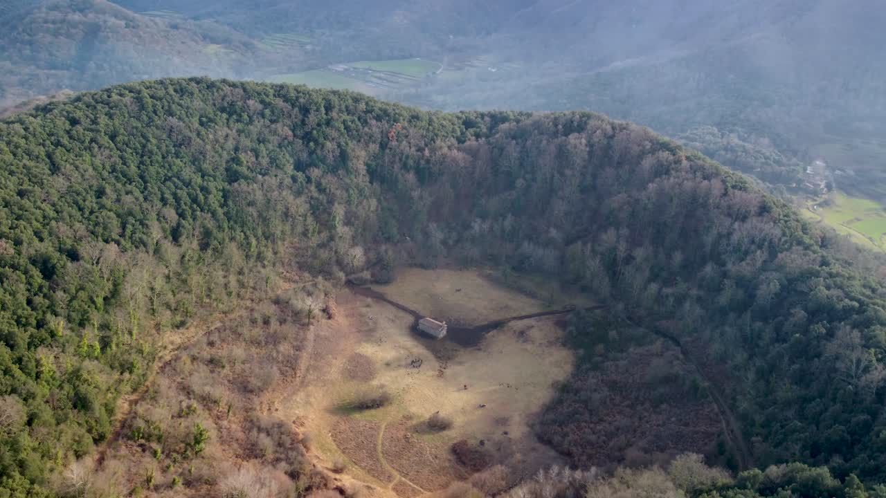 círculo aéreo lento alrededor del volcán inactivo de santa margarida: enorme cráter y capilla histórica en cataluña, españa