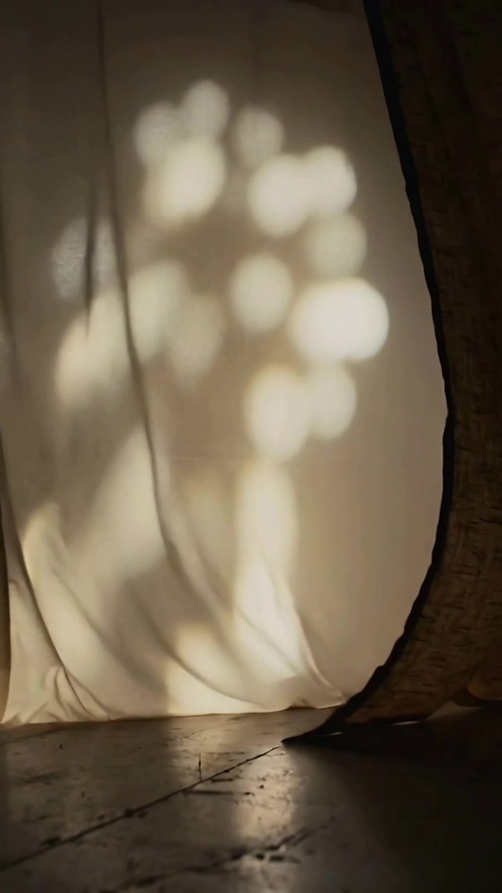 Vertical video: Breeze through gap moving sheer panel by tan panel on floor in room, shifting light