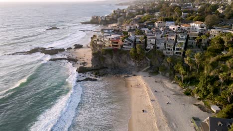 beautiful sandy beach with waves of pacific ocean reaching shore and luxury buildings on top of cliff