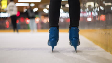 primer plano de alguien patinando en patines azules con pantalones negros en una pista de hielo, la escena captura un movimiento a lo largo de la pista