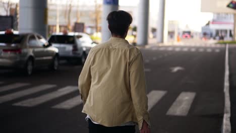 Hombre-Alto-Y-Seguro-De-Sí-Mismo-Con-El-Equipaje-Negro-Caminando-Hacia-La-Terminal-Exterior-Del-Aeropuerto-Por-Carretera