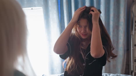 girl in black pajamas sitting on bed holding remote as microphone while singing with dramatic facial expression during playful moment indoors