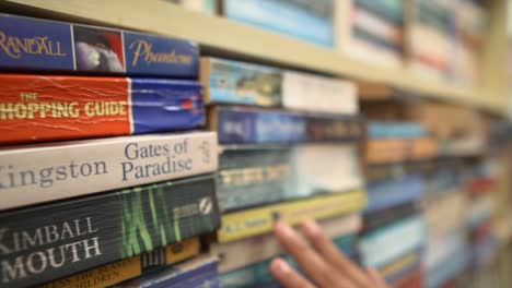 Close-up-shot-of-young-woman-hand-exploring-books-through-bookshelves