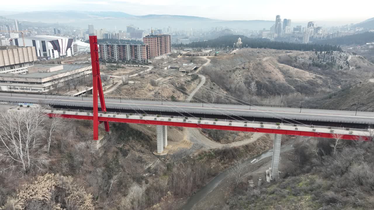 A red bridge amidst an urban frozen landscape. The architecture contrasts with the muted tones of the surrounding winter setting, showcasing the intersection of city life and nature