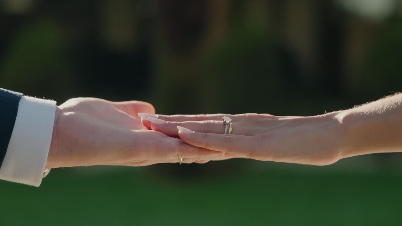 Bride and groom gently touch fingertips, highlighting wedding rings in soft light