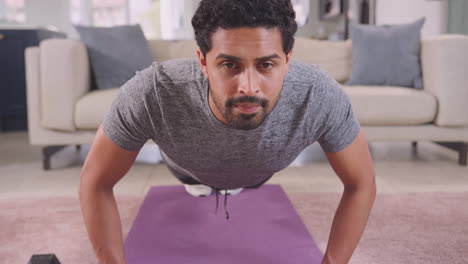 camera follows man in fitness clothing up and down as her does press ups on mat in lounge at home - shot in slow motion