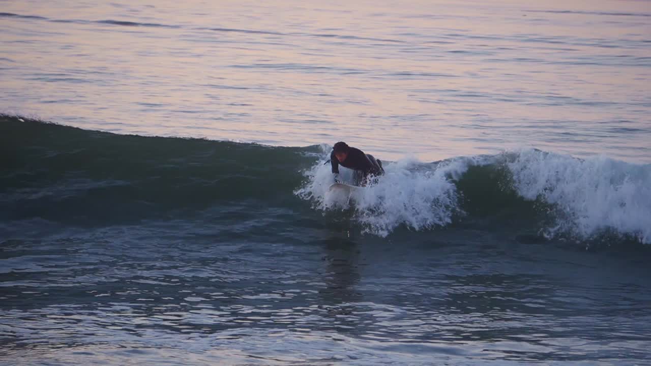 Giovane che fa surf all'alba eseguendo acrobazie con una tavola da surf