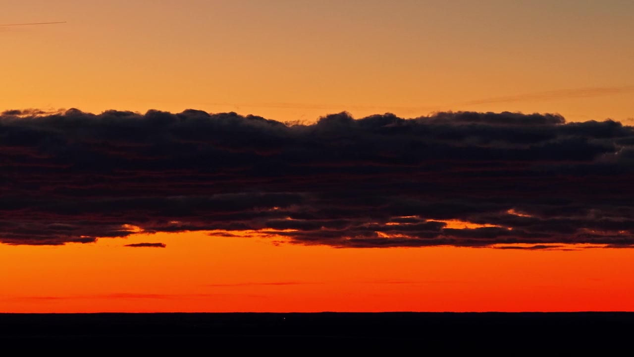 Dramatischer roter Sonnenuntergang über dem Horizont mit dunklen Wolken und orangefarbenem Himmel in der Luftaufnahme.