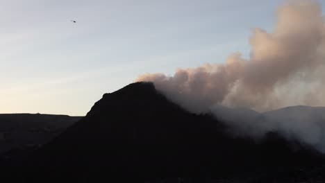 helicopter flying over smoking volcano cone iceland