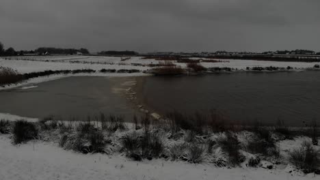 panorama of a countryside by a calm lake during snowfall in winter