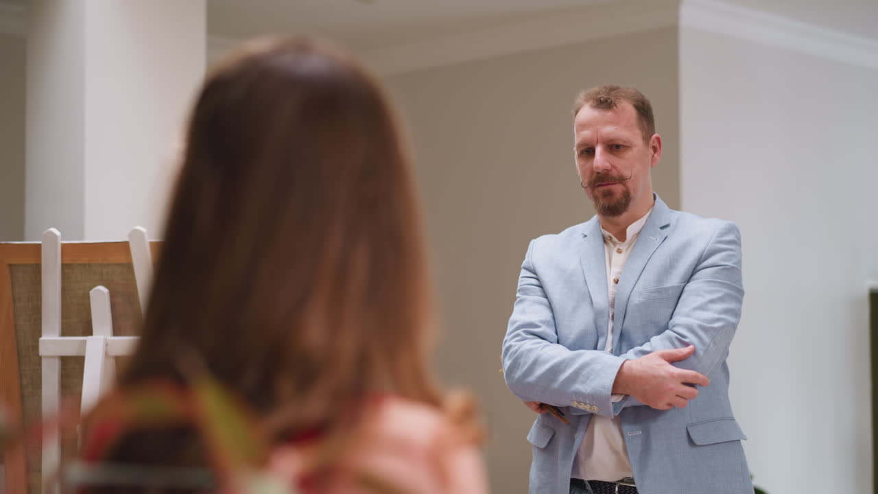 el artista asenta con la cabeza mirando a la modelo en el estudio. el pintor talentoso con los brazos cruzados aprueba la pose de la mujer para el retrato en la tienda de arte. el creador en el trabajo