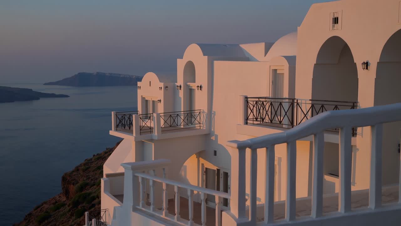 Traditional whitewashed hotel in Santorini, Greece, basking in the warm glow of the setting sun, offering breathtaking views of the Aegean Sea and volcanic caldera
