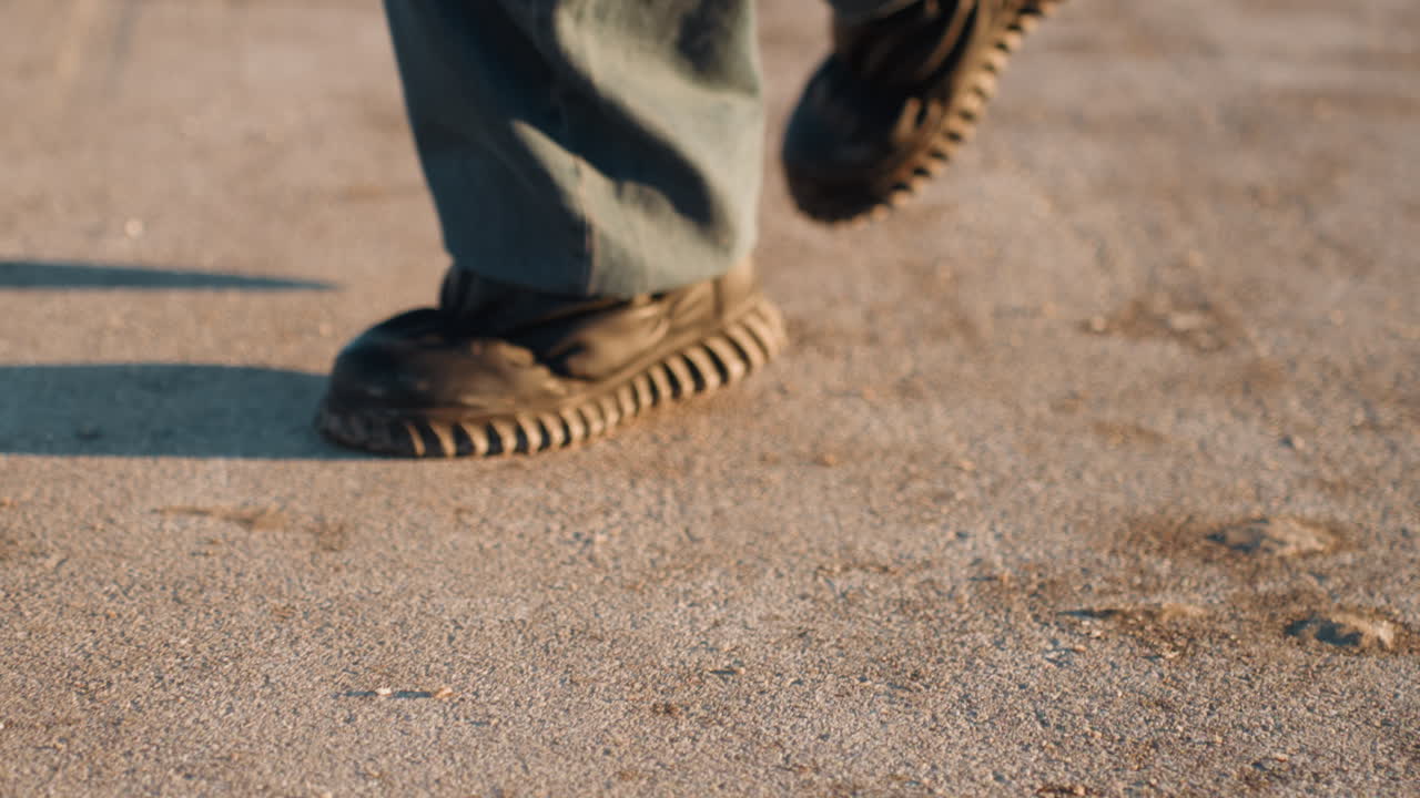 Vorsichtiges Gehen über frostiges Pflaster. Nahaufnahme von Schuhen, die strukturierte Abdrücke auf gefrorenem Boden bei Sonnenuntergang hinterlassen. Detaillierte Aufnahme von Stiefeln, die auf einer eisigen Oberfläche auf einem Dach zur goldenen Stunde gehen.