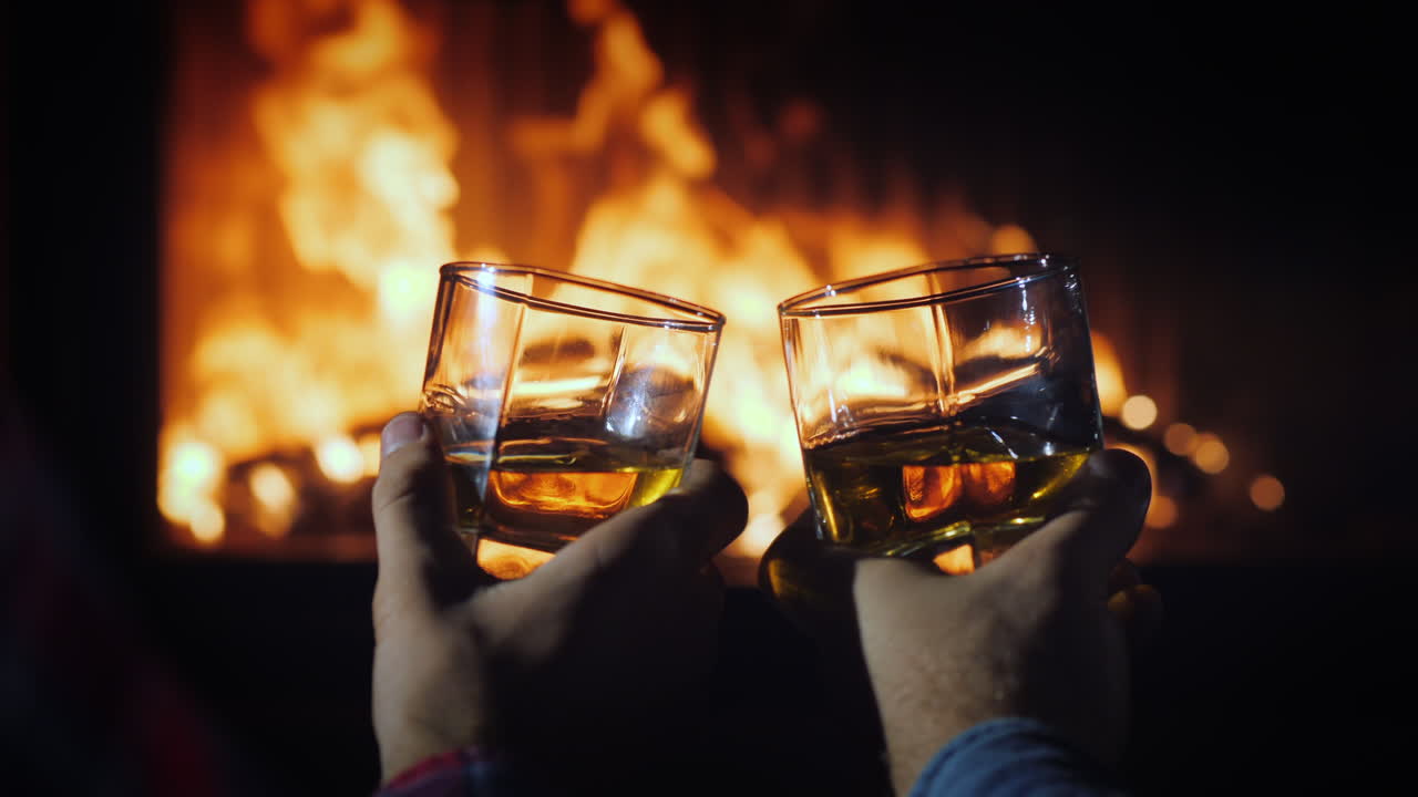 dos manos masculinas con vasos de whisky con hielo en el fondo de la chimenea escape de invierno con