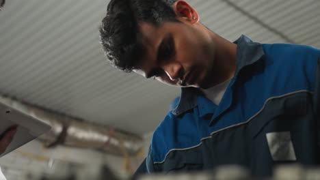 boy working on tablet in industrial workshop while another man focuses on task, background features workshop equipment, tools, and machinery