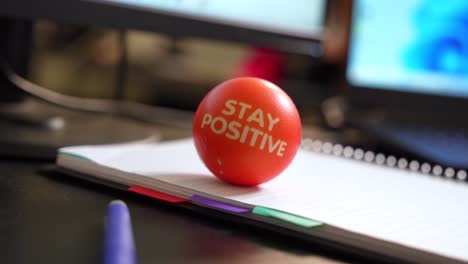 orange stress ball with "stay positive" text on a notebook in office setting. perfect for motivation, workplace, or mental health themes.
