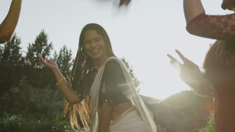 Two happy Indian women dancing in traditional attire outdoors in a sunny garden