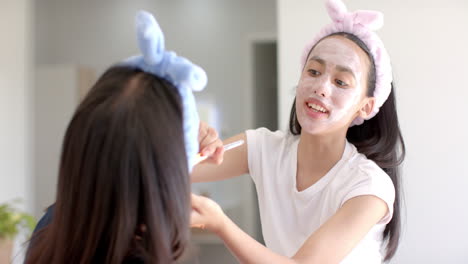 biracial teenage girl pals in animal ear bands apply face masks at home