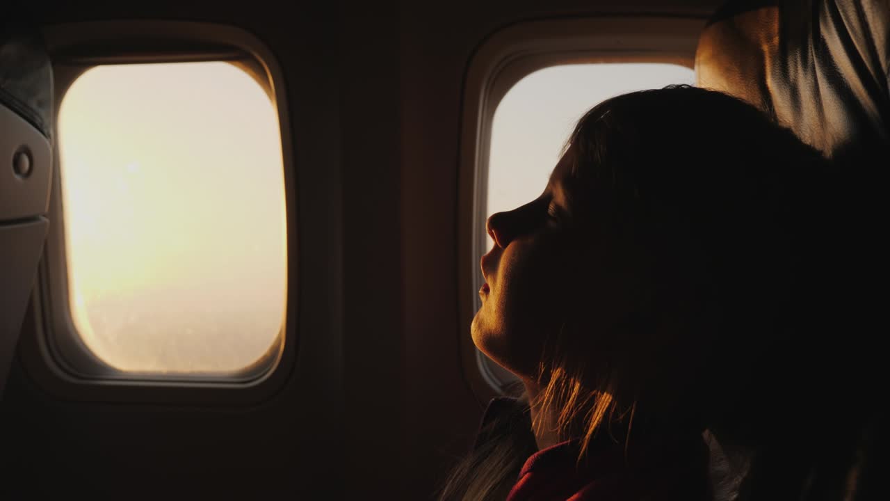 비행기에서 자고 있는 아이의 실루, 창밖에서 해가 뜨고, 아이들과 함께 여행하는 개념