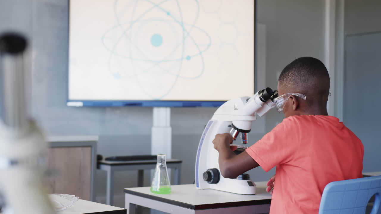 In school, boy using microscope and examining sample in science classroom