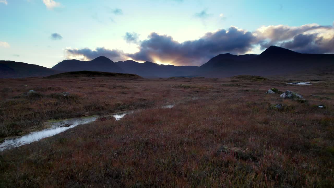 imágenes aéreas de drones volando bajo y cerca de la superficie de una turbera hacia montañas oscuras en el horizonte al atardecer
