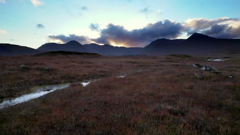 Drohnenaufnahmen-Aus-Der-Luft,-Die-Bei-Sonnenuntergang-Tief-Und-Nahe-An-Der-Oberfläche-Eines-Torfmoors-In-Richtung-Dunkler-Berge-Am-Horizont-Fliegen