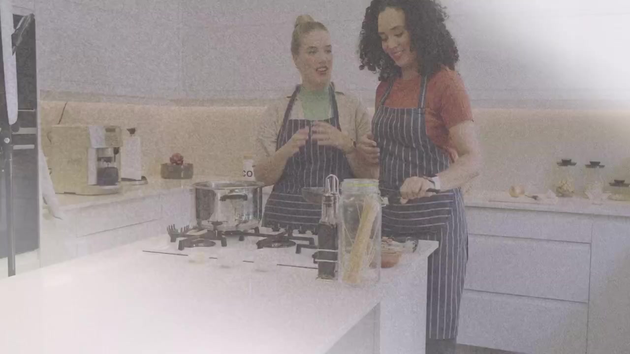 Due donne che applaudono e sistemano pentole sul fornello a gas, mettendo pasta e olio per cucinare.